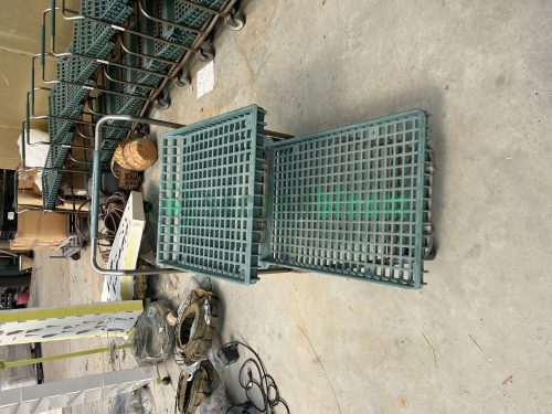 Front view of a used two-level nursery shopping cart with green hard plastic shelves featuring square holes.