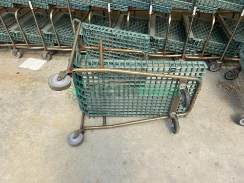Upside down view of a used two-level nursery shopping cart, revealing the construction of the green hard plastic shelves and metal frame.