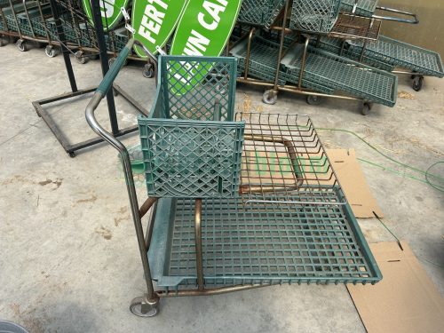 Side view of a used two-level nursery shopping cart, highlighting the ergonomic handle and four sturdy wheels.