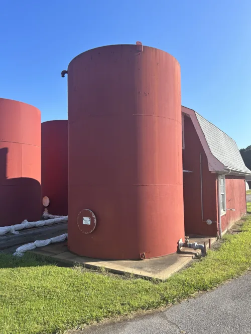 Large red industrial storage tank positioned in front of a shed.