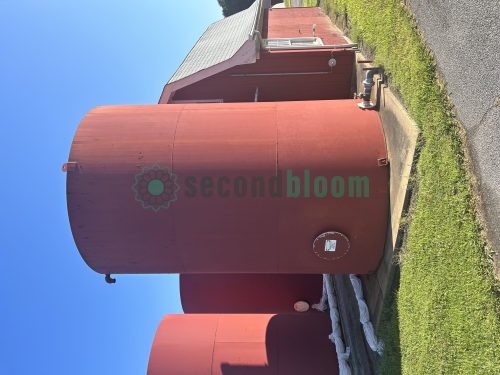 Large red industrial storage tank positioned in front of a shed.