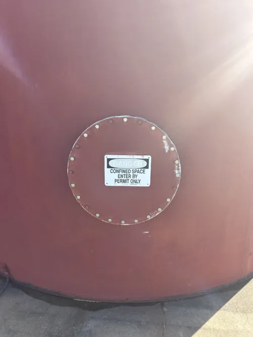 Close-up view of a warning label on a large red industrial storage tank.