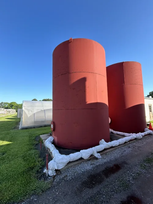 Two large red industrial-grade storage tanks standing side by side outdoors.