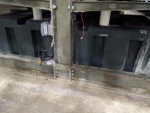 Close-up view of the base structure of a vertical farm system at Your Local Greens in Burlington, NC, highlighting the water storage tank and electrical connections.