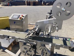 Close-up view of a Pack Leader PL-221 labeling machine, used in leafy greens packaging, showcasing conveyor belt, labeling mechanism, and control panel near Gonzales, California.