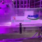 Hamill APS logo on a clear plastic safety shield over the conveyor belt of a microgreen harvester