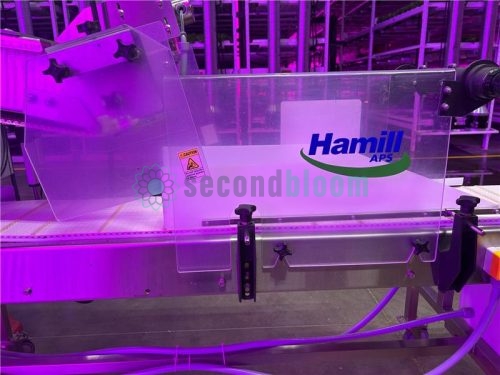 Hamill APS logo on a clear plastic safety shield over the conveyor belt of a microgreen harvester