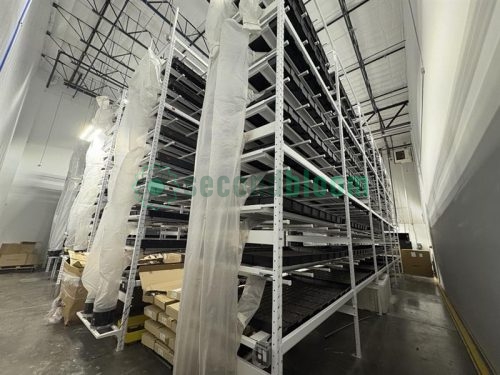 Large-scale vertical grow racks wrapped in protective plastic sheeting, ready for disassembly in an industrial warehouse.