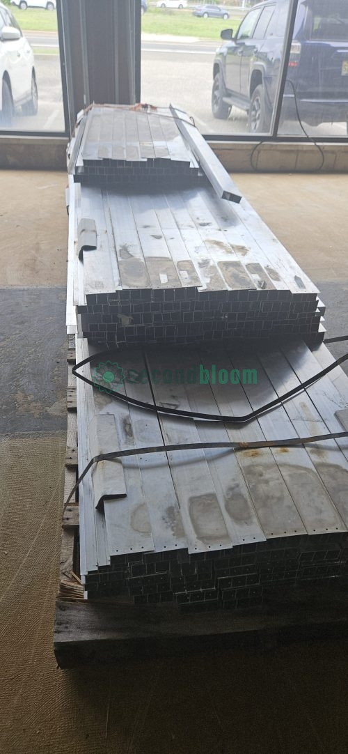 Side view of warehouse showing stacked galvanized steel components for greenhouse benches with large windows and metal framing