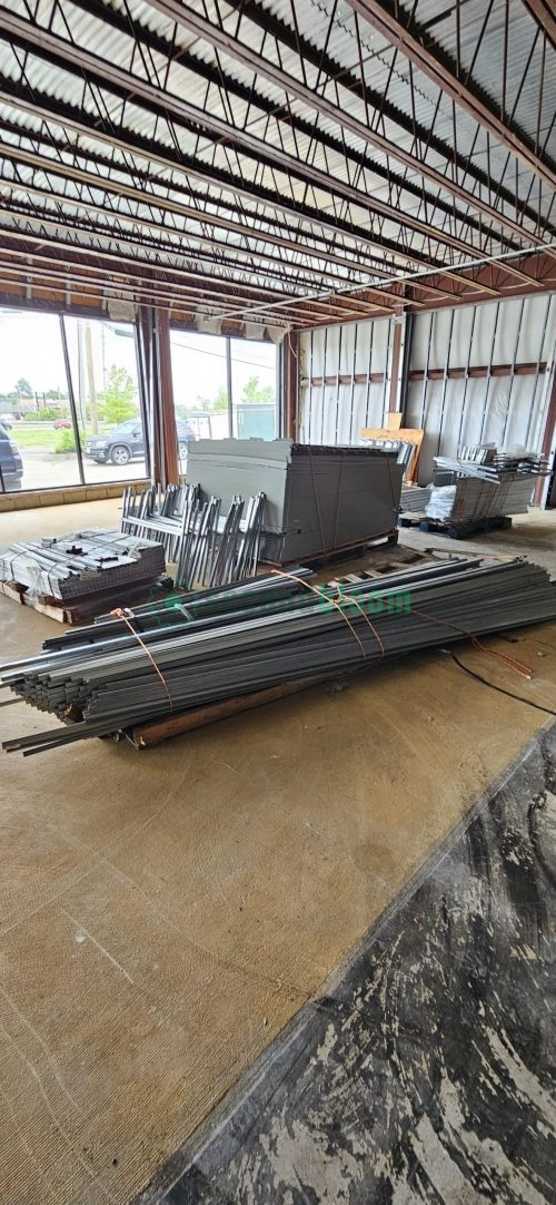 Stack of galvanized and aluminum greenhouse bench components with white PVC fittings on concrete floor in warehouse