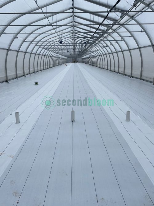Interior view of assembled Harnois Ovaltech greenhouse showing white flooring, arched metal framework, and translucent covering with excellent height clearance