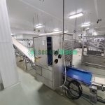 Roopack branded filling equipment with stainless steel perforated panels and conveyor system in food processing facility
