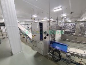 Roopack branded filling equipment with stainless steel perforated panels and conveyor system in food processing facility