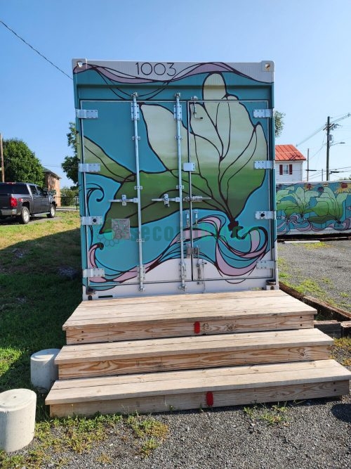 Rear cargo doors of container unit 1003 painted with large green tropical leaves and turquoise swirling water patterns on wooden platform with steps