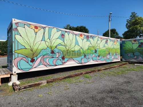 Extended side view of container farm showing repeating pattern of large green water lily plants with yellow and purple flowers against light blue corrugated walls