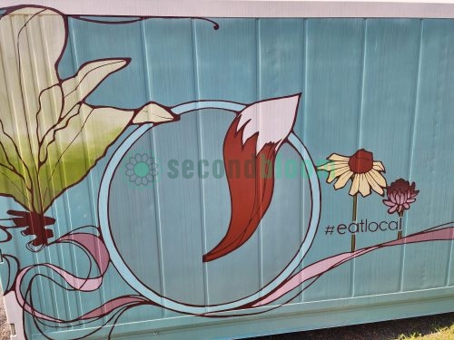 Close-up of container farm mural showing large green aquatic plants with red roots, pink water swirls, and flowers with #eatlocal hashtag on blue background