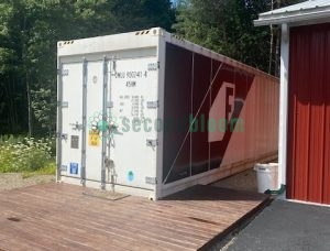 Exterior view of white 40-foot shipping container with open side panel revealing farming equipment, positioned on wooden platform